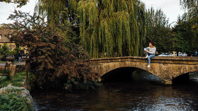 Woman sitting on a low stone bridge over a river in a village