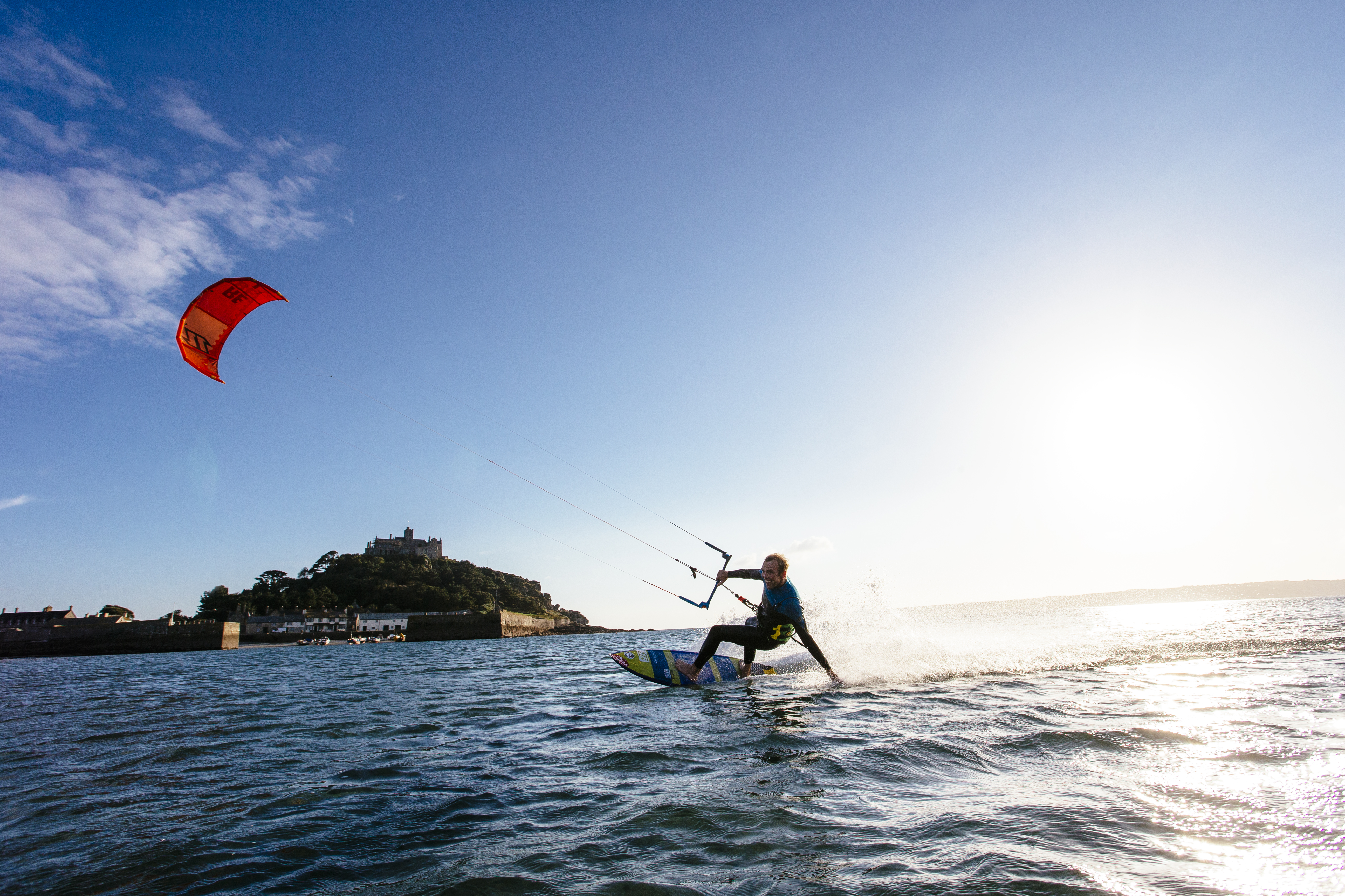 Un hombre sobre una tabla de surf sujetando la barra de control de una cometa