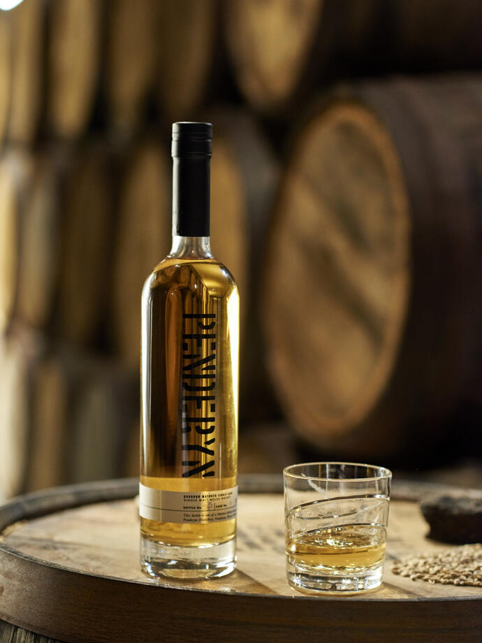 Une bouteille de whisky et un verre de whisky posés sur un tonneau en chêne