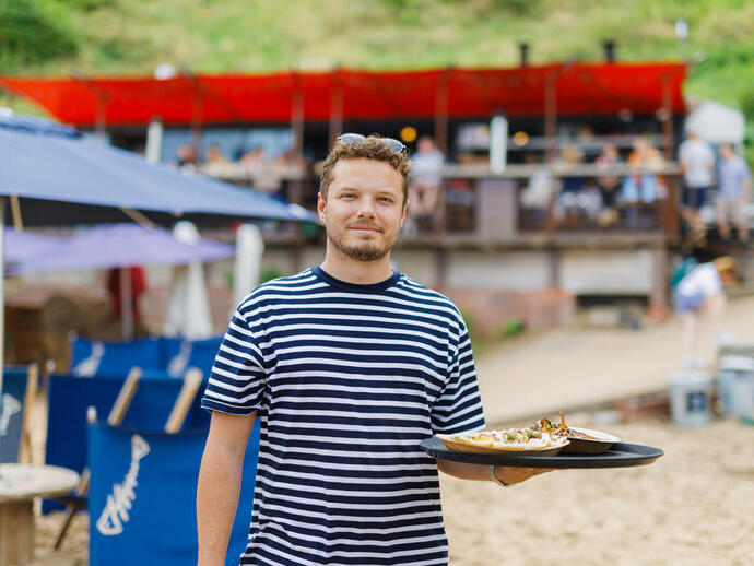 Member of staff of a beach café and restaurant holding a tray of food