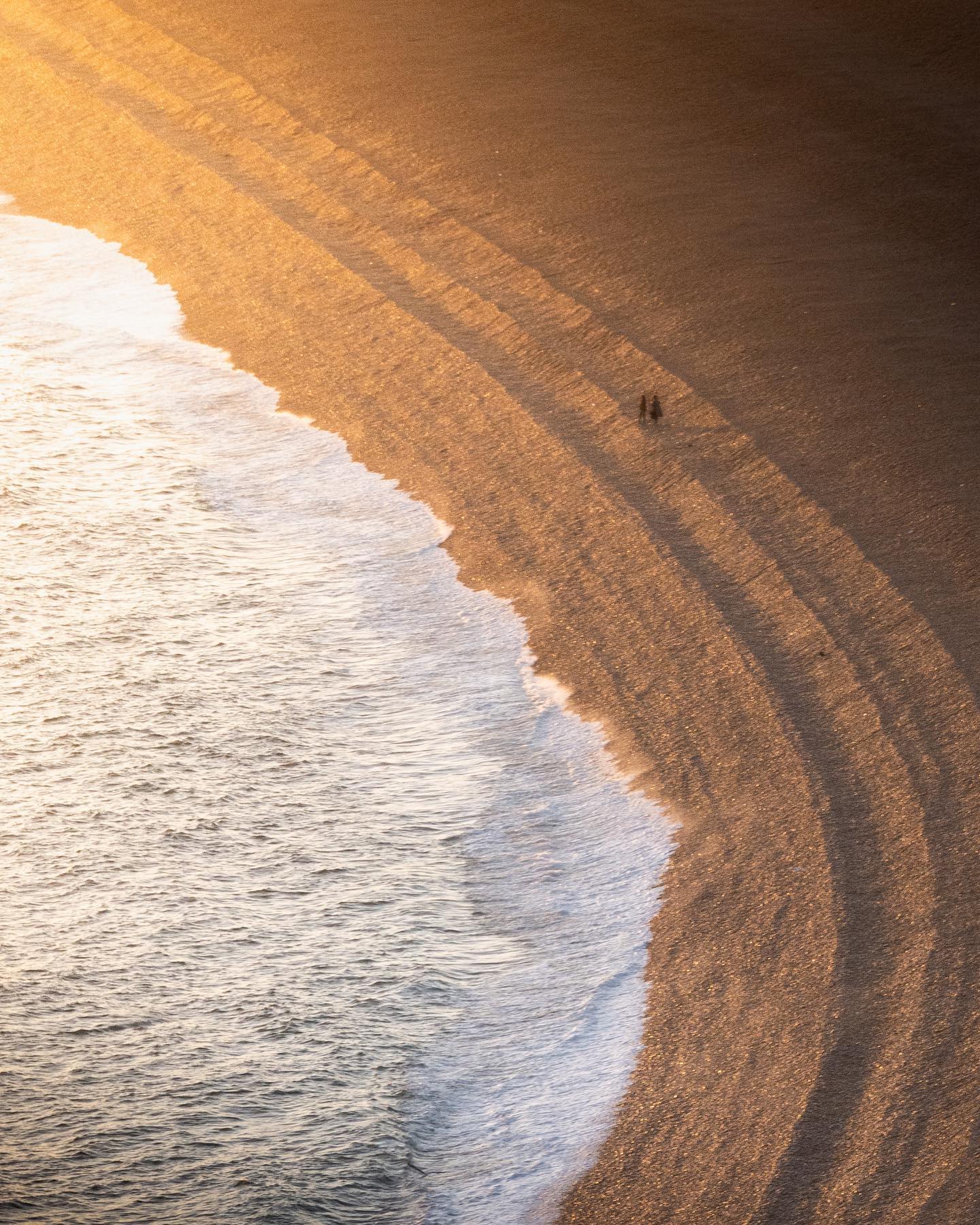 Aerial of two people on the sea shore at sunset