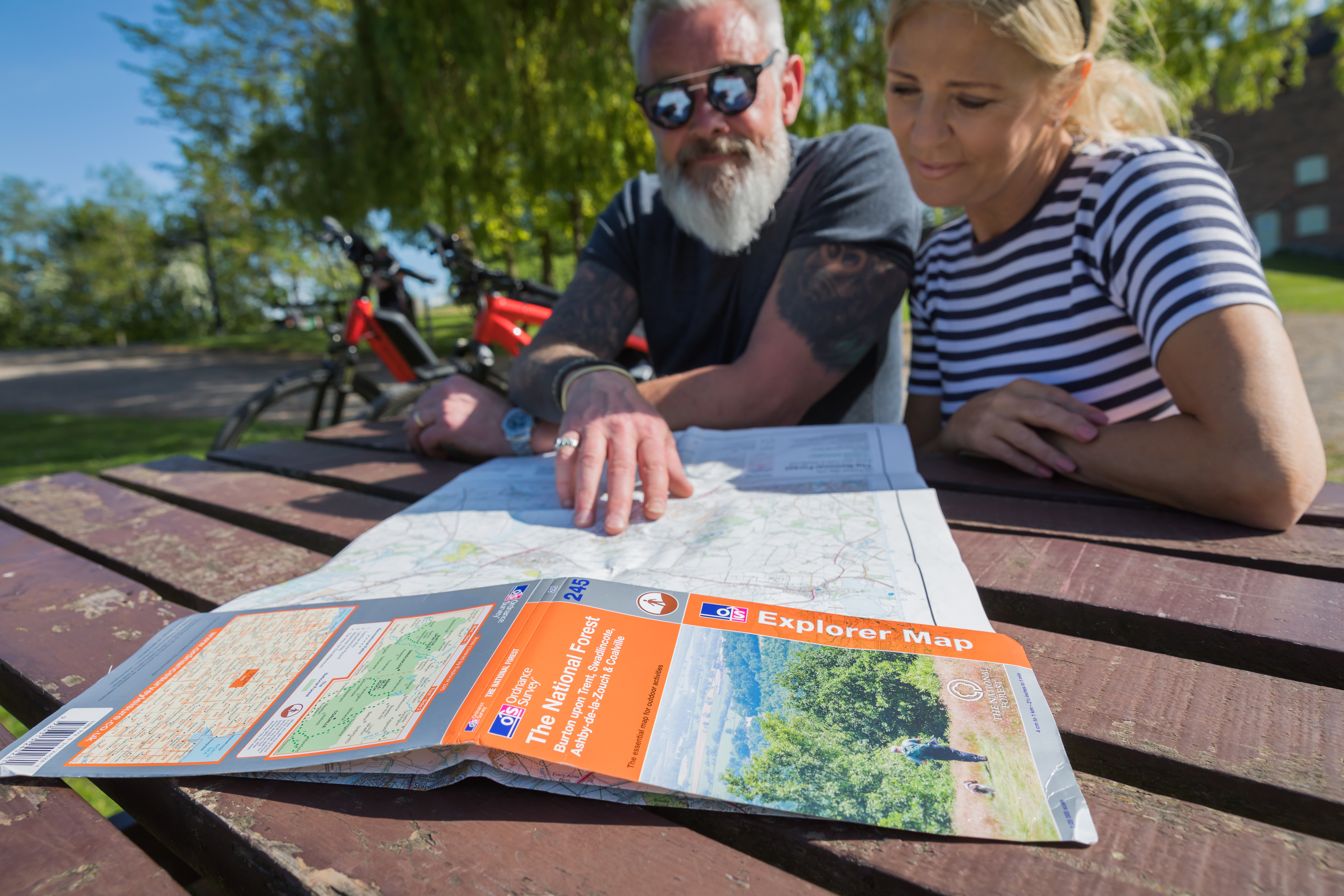 Two people sat at a picnic table, looking at an Ordinance Survey Explorer map of the National Forest.