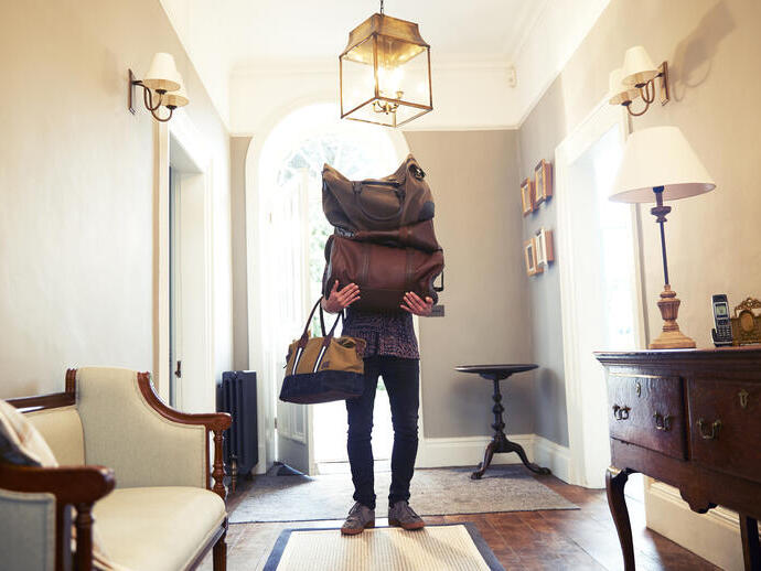 Man entering a beautiful hallway holding luggage covering his face and upper body
