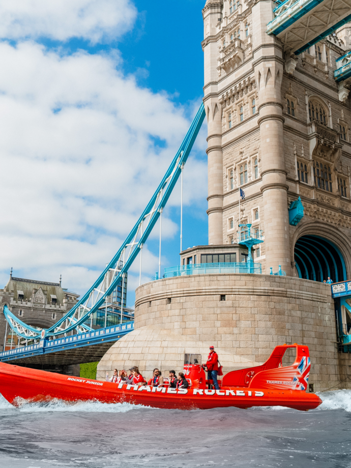 A speedboat with tourists zipping past Tower Bridge