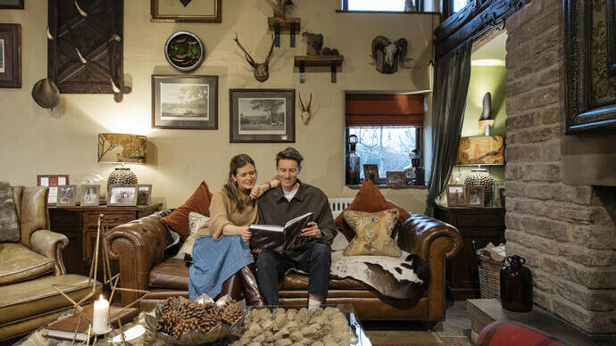 Cozy living room with a couple reading on a leather sofa, surrounded by eclectic decor and warm lighting.