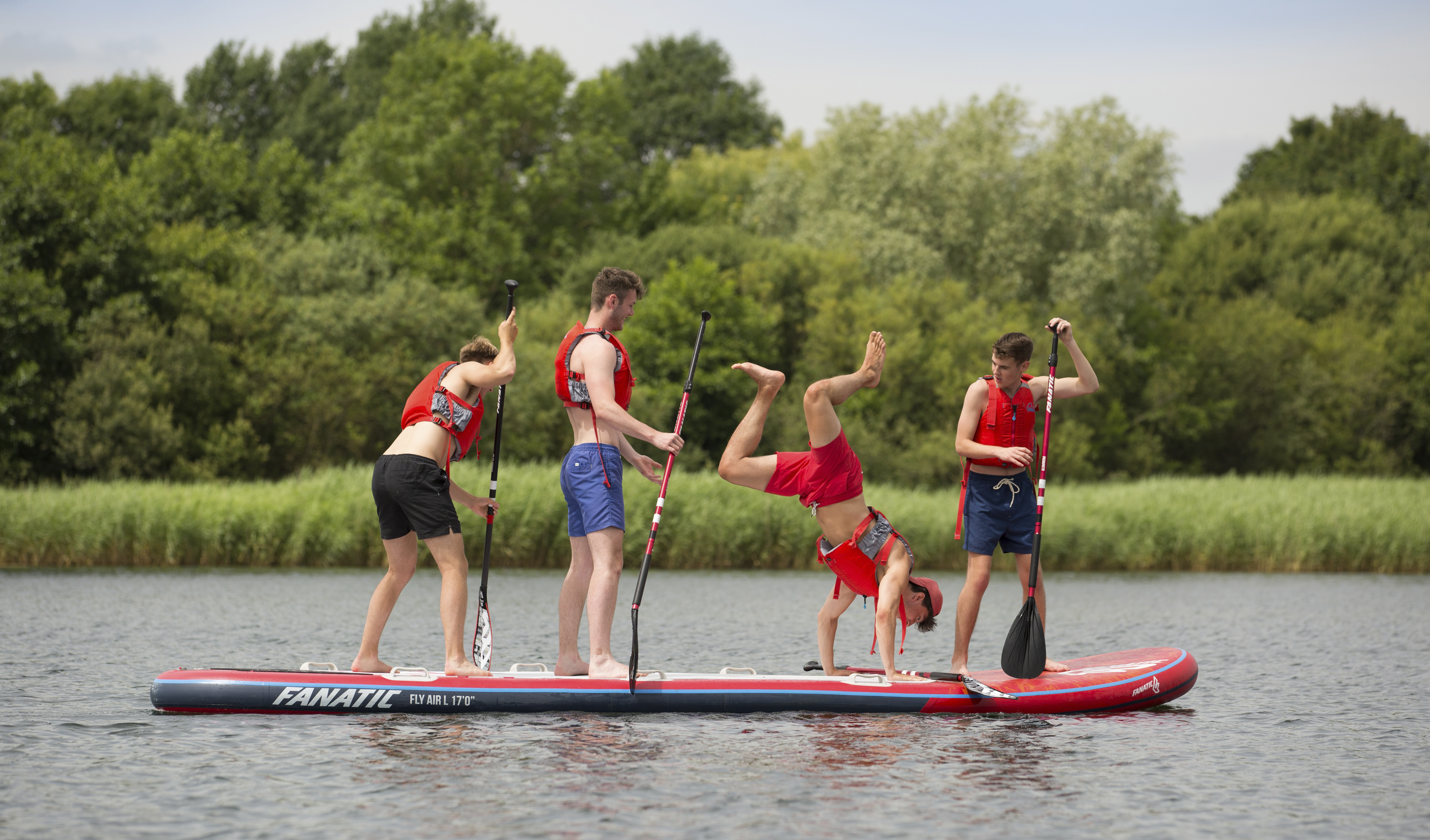 Four men in red life vests standing on a paddleboard