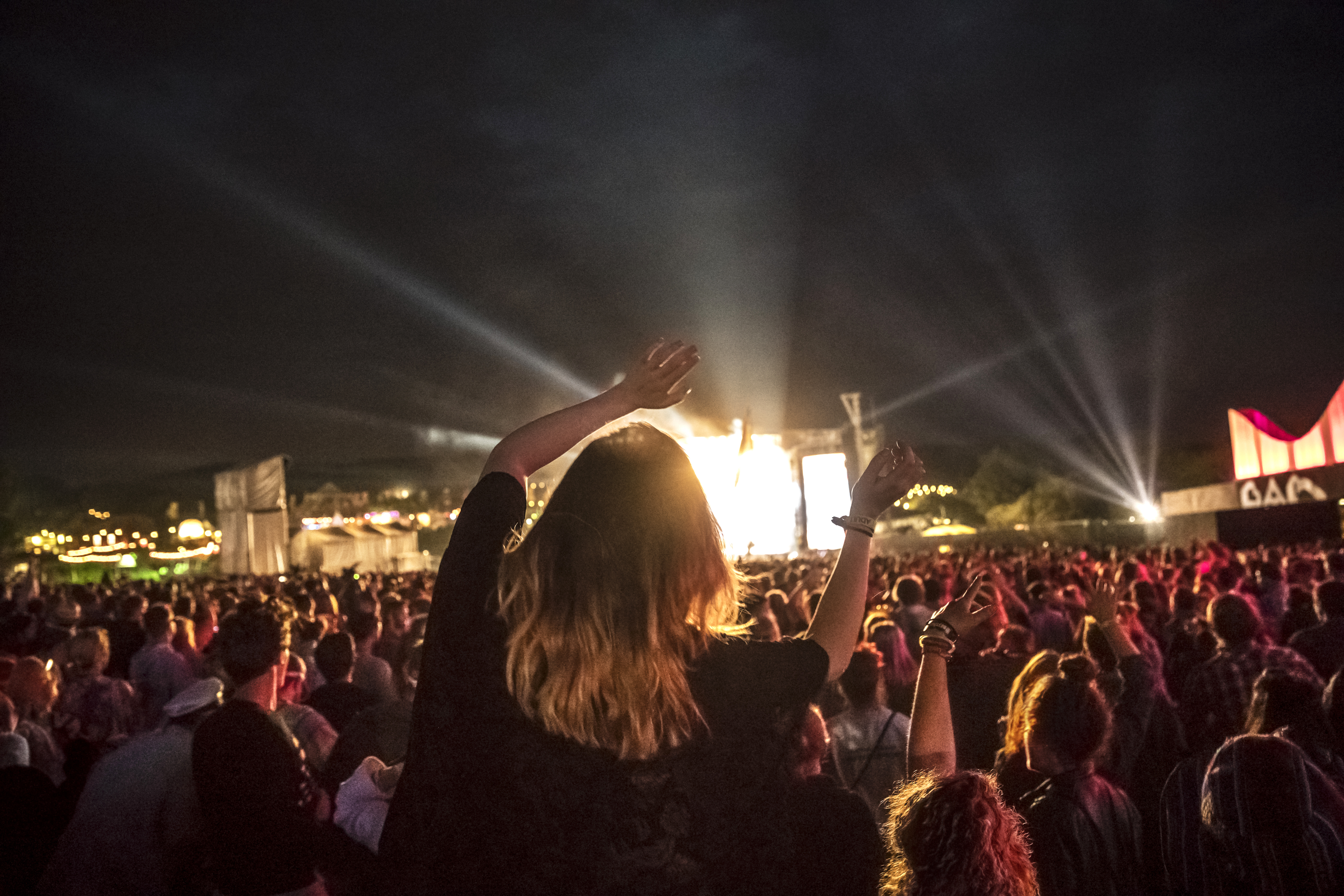 Woman in the crowd at a music concert with her arms in the air watching a performance