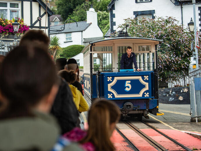 A line of people at a station queuing for a blue tram.
