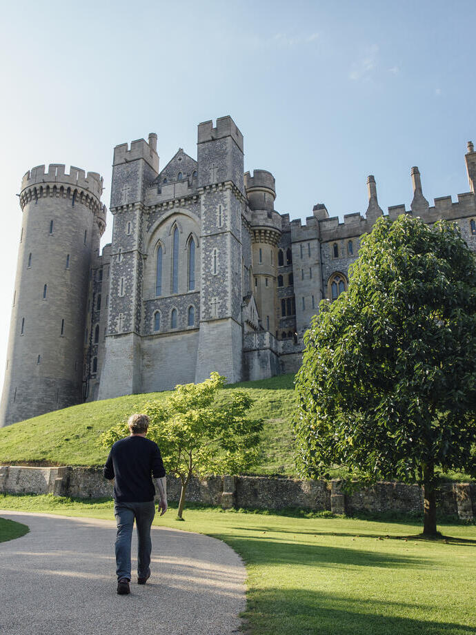 Man walking on a path towards a large medieval castle.