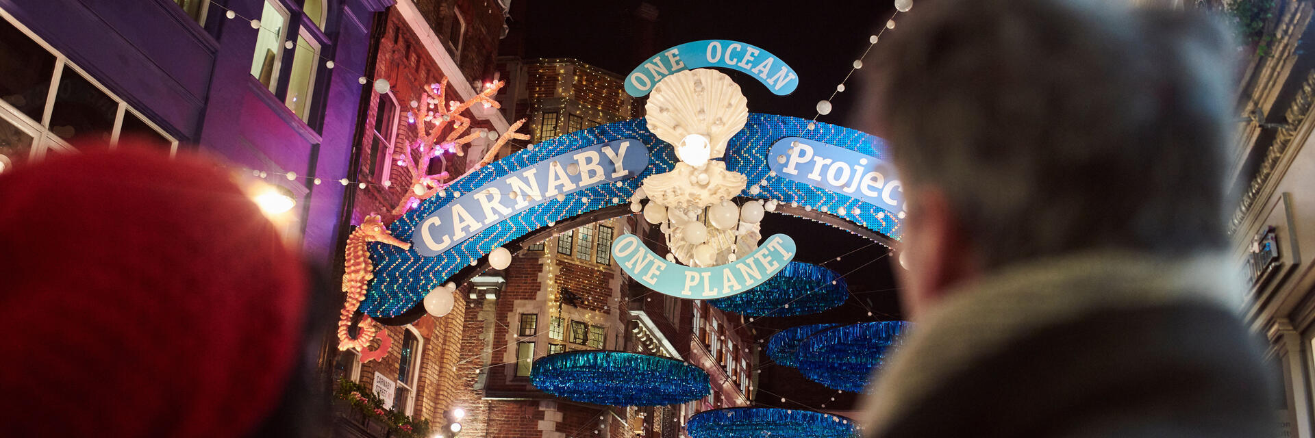 زوجان ينظران إلى أضواء الشوارع وزينة عيد الميلاد ولافتة شارع كبيرة