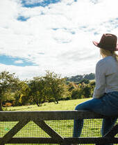 Woman sitting on a wooden gate looking across a field