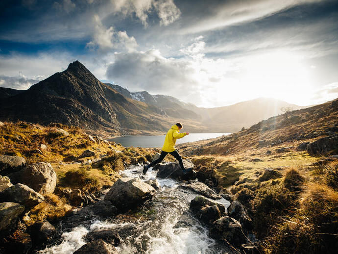 Man jumping from rock to rock across a stream flowing into a lake