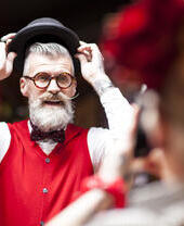 Quirky vintage wearing woman photographing friend trying on bowler hat in antiques emporium.