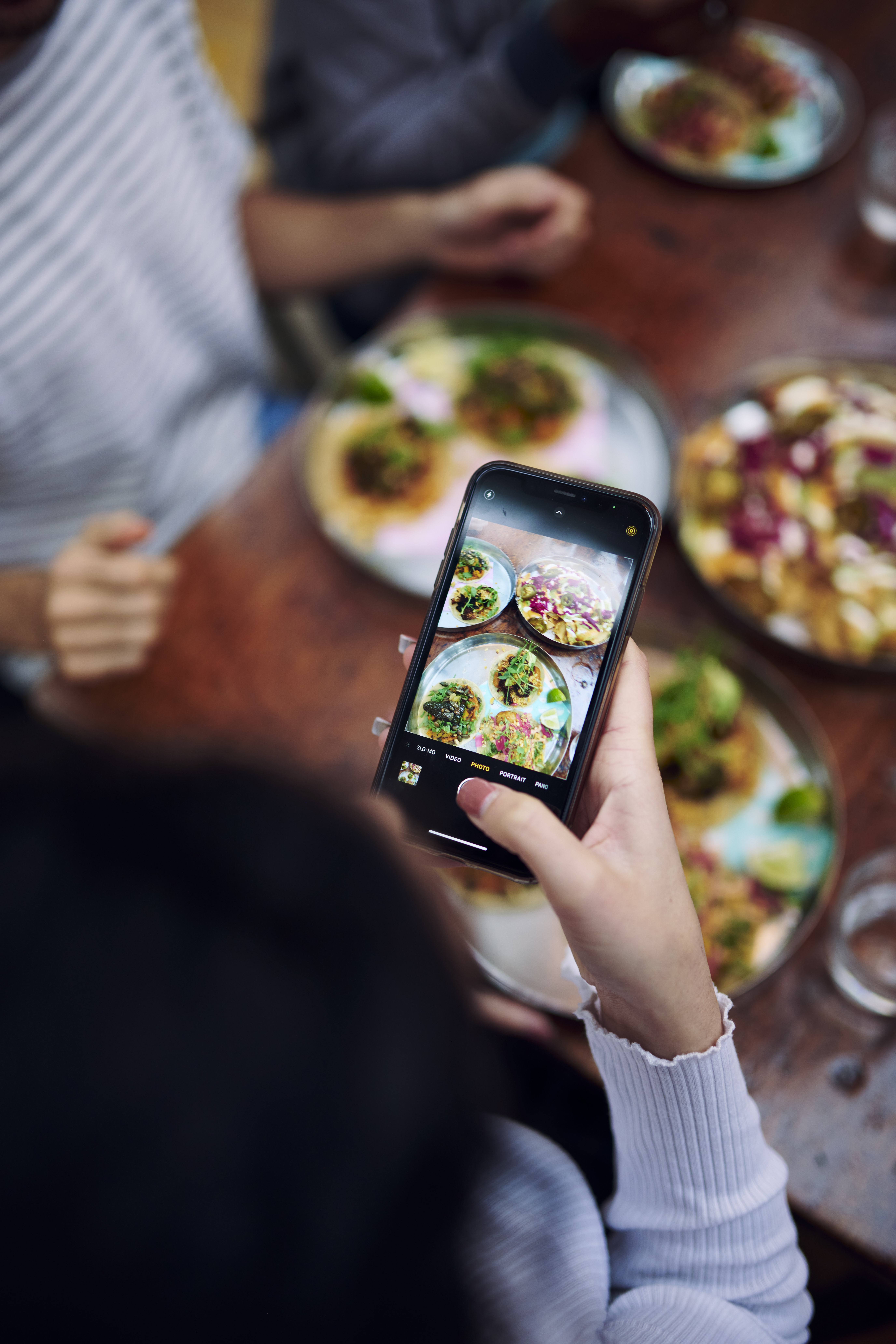 Woman taking a photo on her mobile phone of food on the table in a restaurant