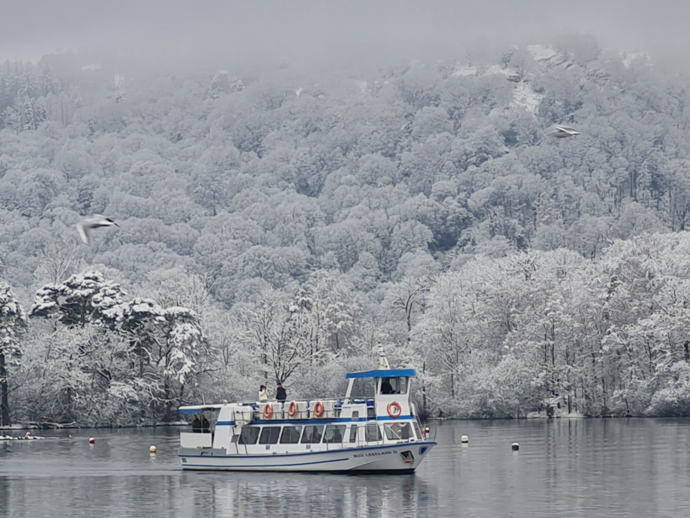 Boat on calm lake with snowy forested hills in the background, wintery and misty atmosphere.