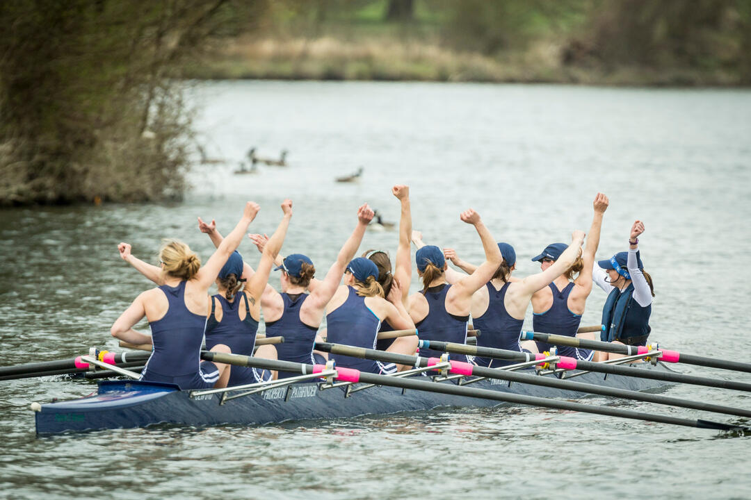 An Oxford University rowing team celebrating while rowing down the River Thames in Oxford