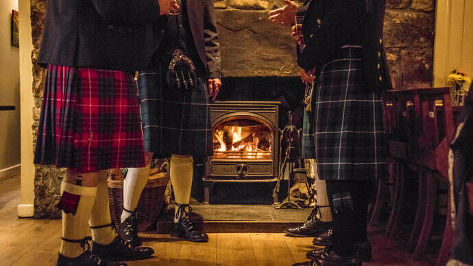 Men wearing kilts standing and drinking by a fireplace in a pub
