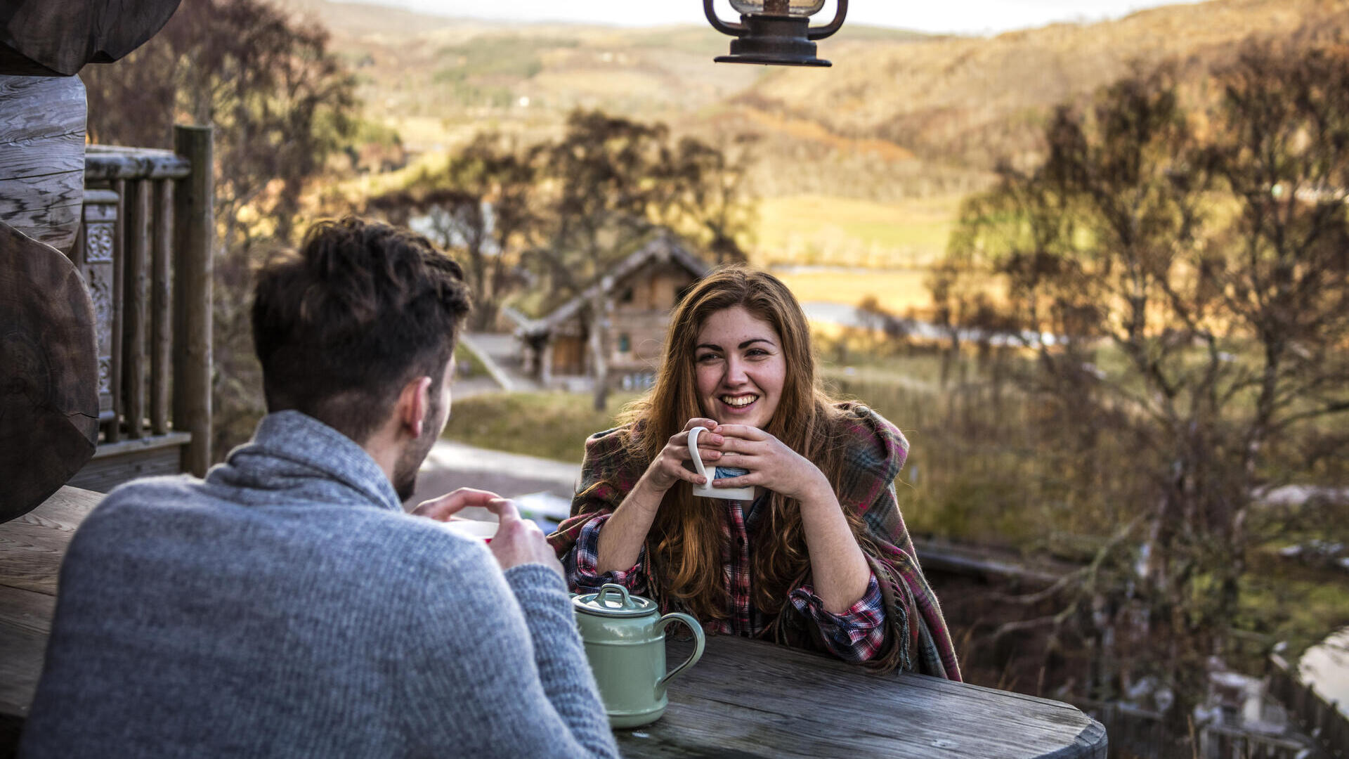 Couple sat at a wooden table drinking tea in a valley