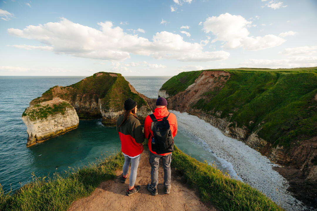 A man and woman stand on a cliff edge in front of a sea view