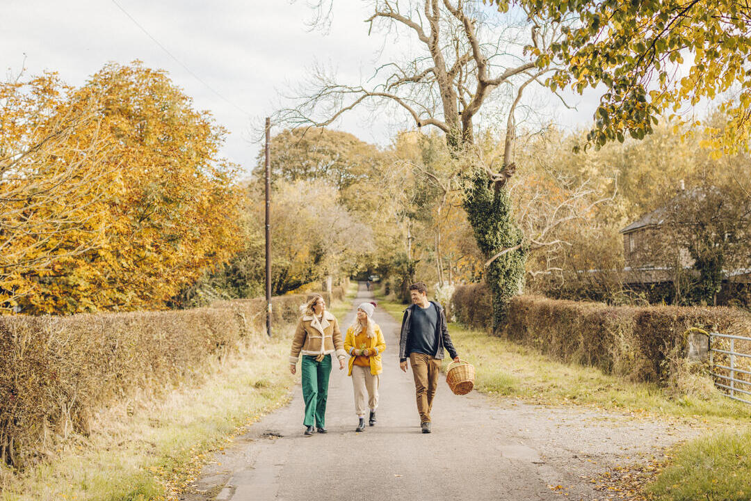 Dos mujeres y un hombre caminando por un camino rural en otoño