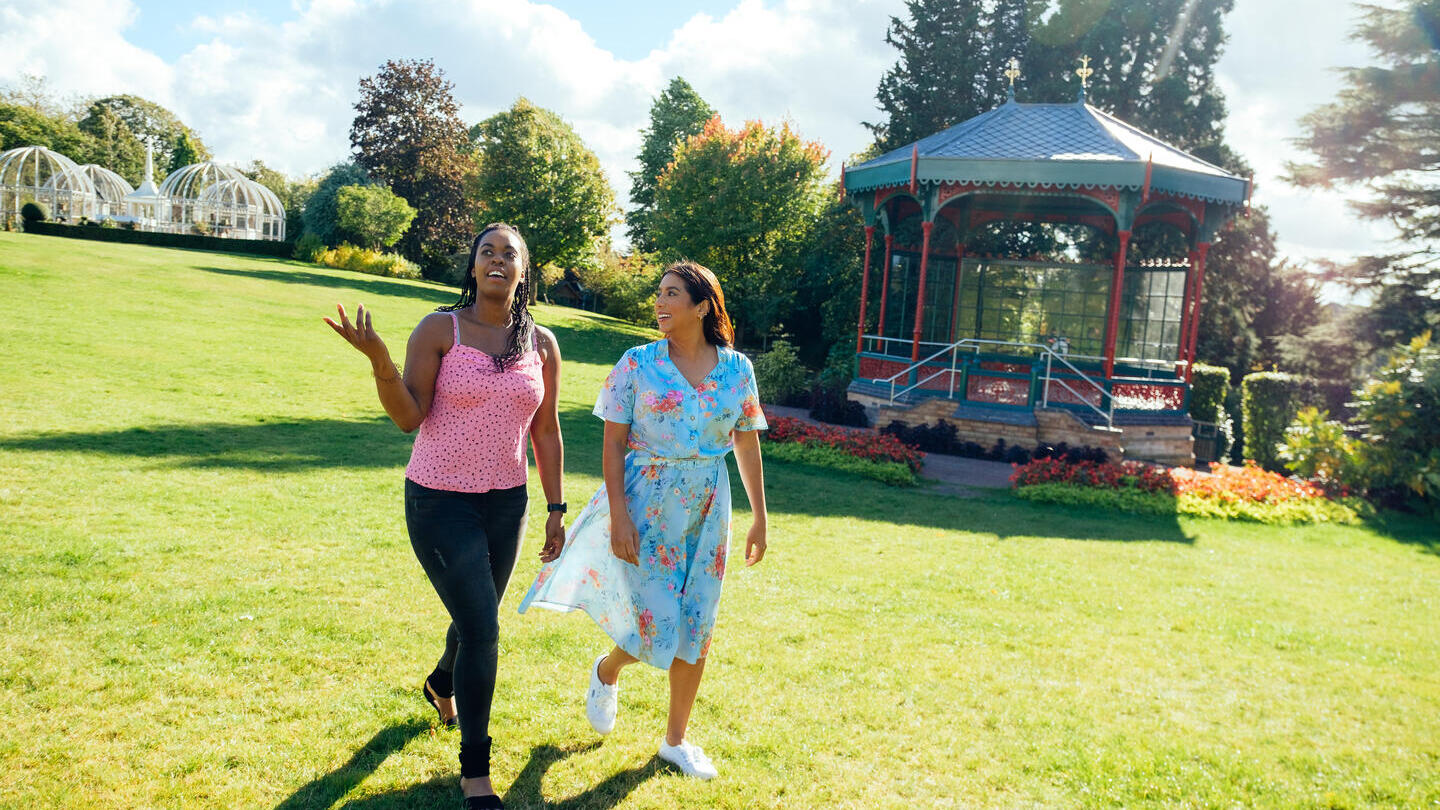 Two women walking on grass past a pergola
