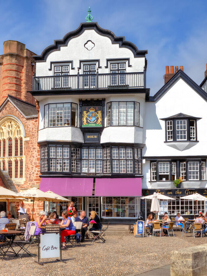 A quaint English town square with outdoor table diners on a sunny afternoon.