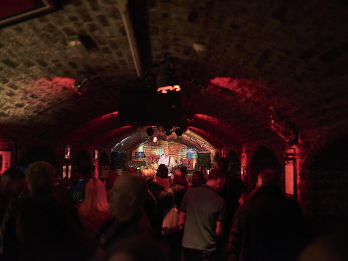 Sala a forma di tunnel in mattoni con un gruppo musicale sul palco.