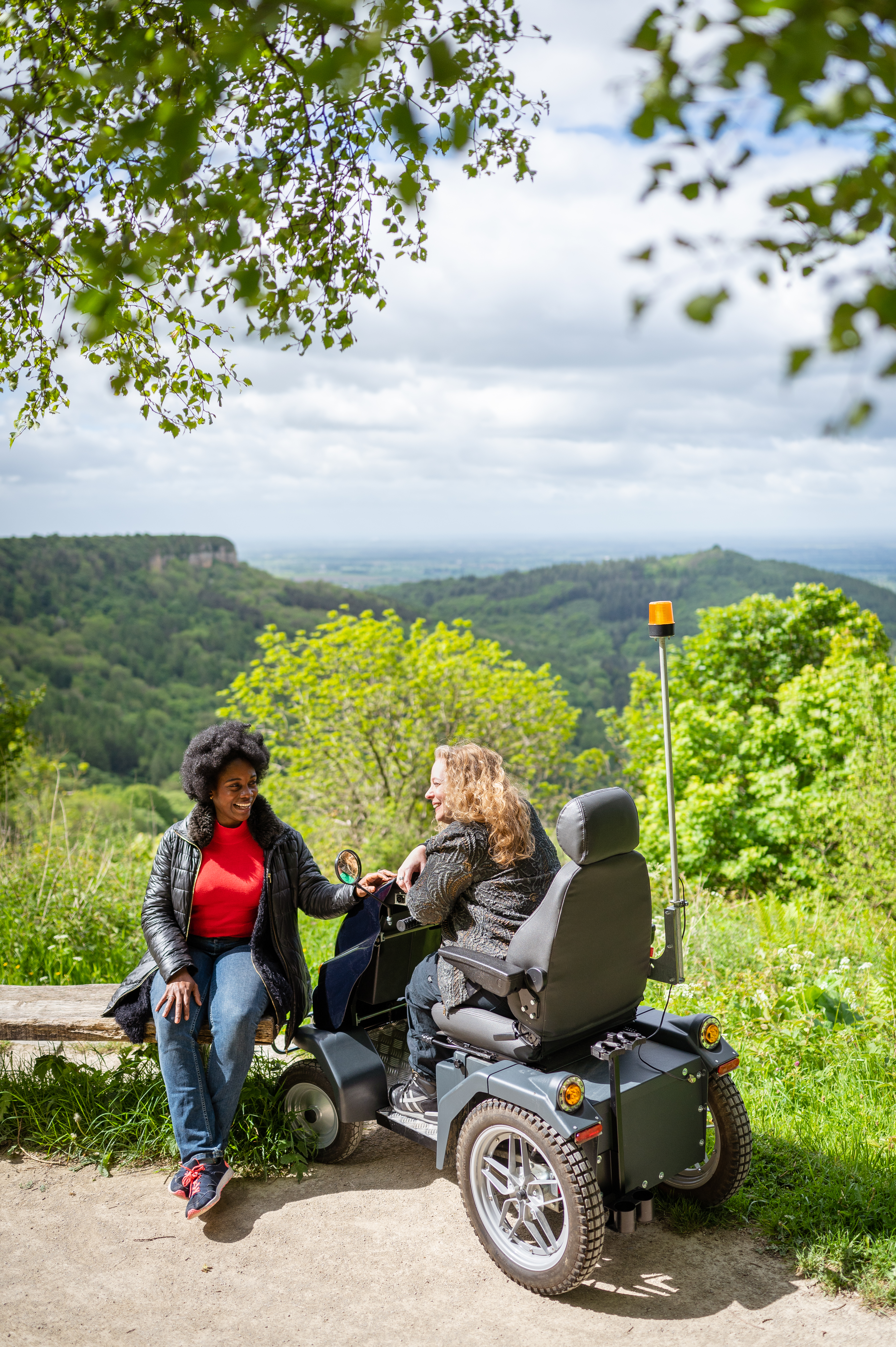 Two women on walking trail, one using a tramper, one sitting on a bench