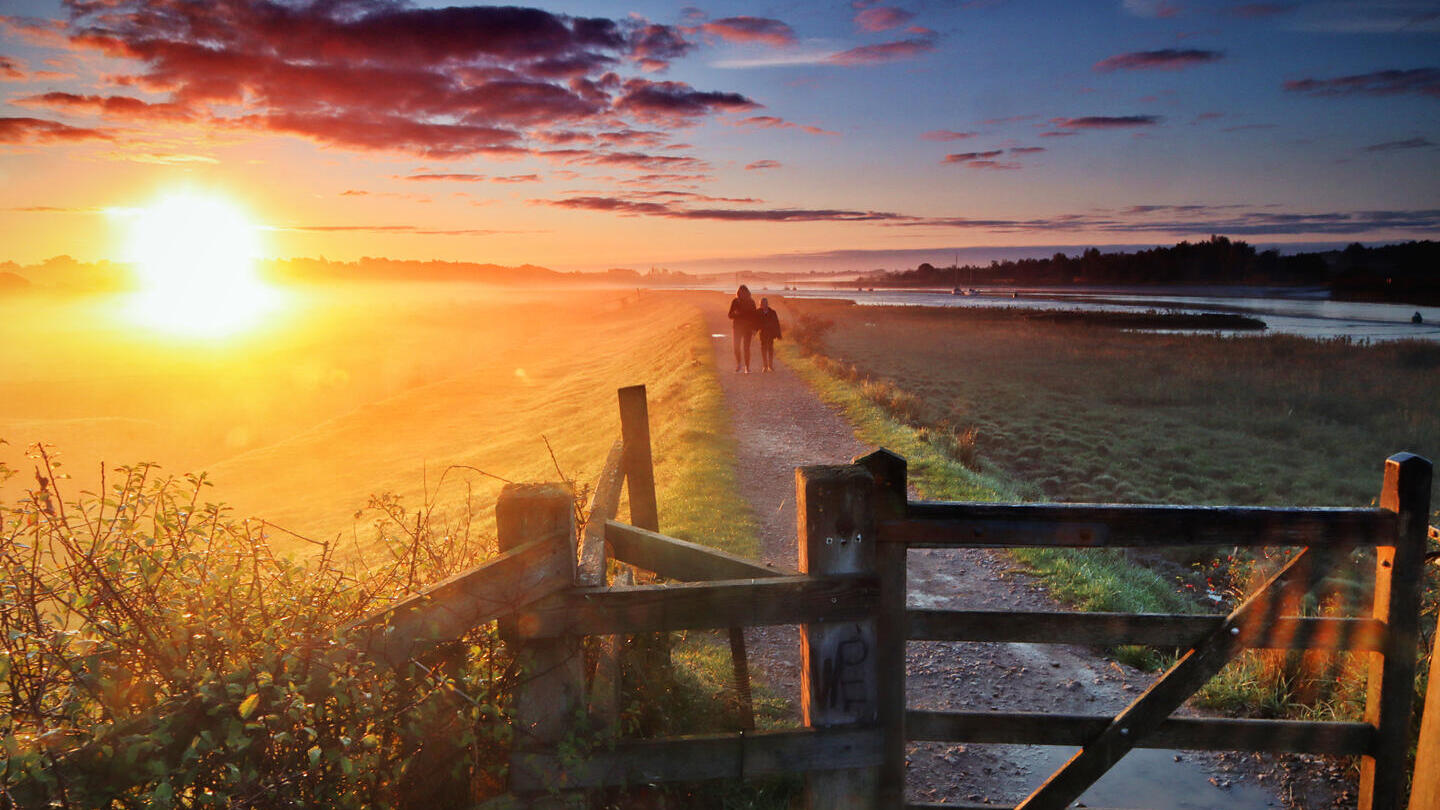 Deux personnes marchant le long d'un sentier au coucher du soleil avec une porte au premier plan