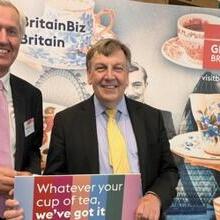 Nick De Bois posing in front of VisitBritain promotional materials