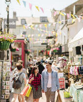 Couple holding hands, walking through a busy pedestrian street with stalls and shops either side