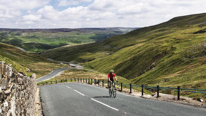 Cyclist riding on road through green dales
