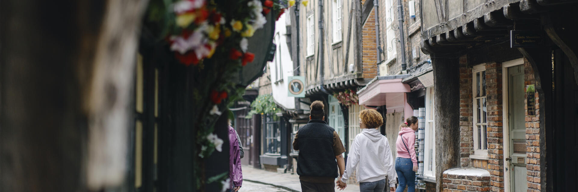A man and a woman walk down a cobbled street holding hands