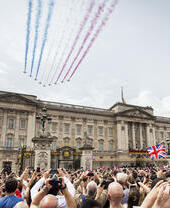 Jets with coloured smoke trailing behind fly in formation over crowds and a palace