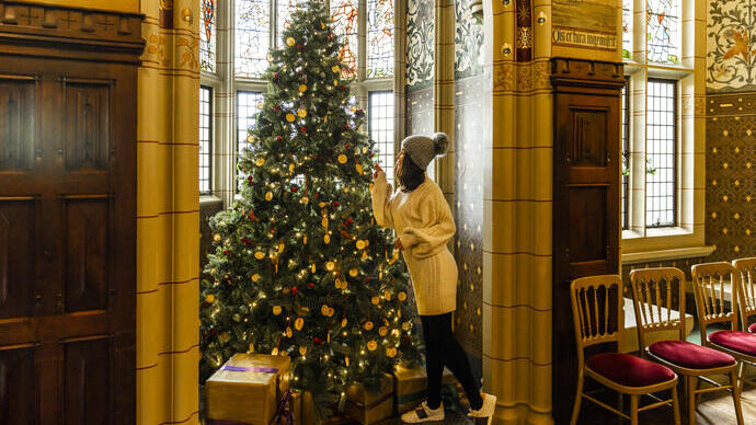 Woman next to a Christmas tree in an historic window bay of a great hall
