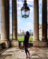 Woman standing underneath a large glass lantern, looking through the colonnades towards modern city buildings