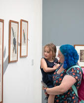 A woman carrying a child, looking at artworks in the Ruskin Collection at the Millennium Gallery in Sheffield