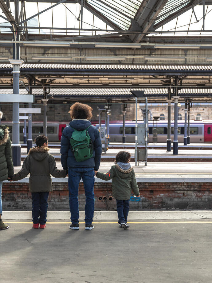 A multiracial family of four, a mother, father and their two little boys standing at Newcastle railway station platform waiting for their train.