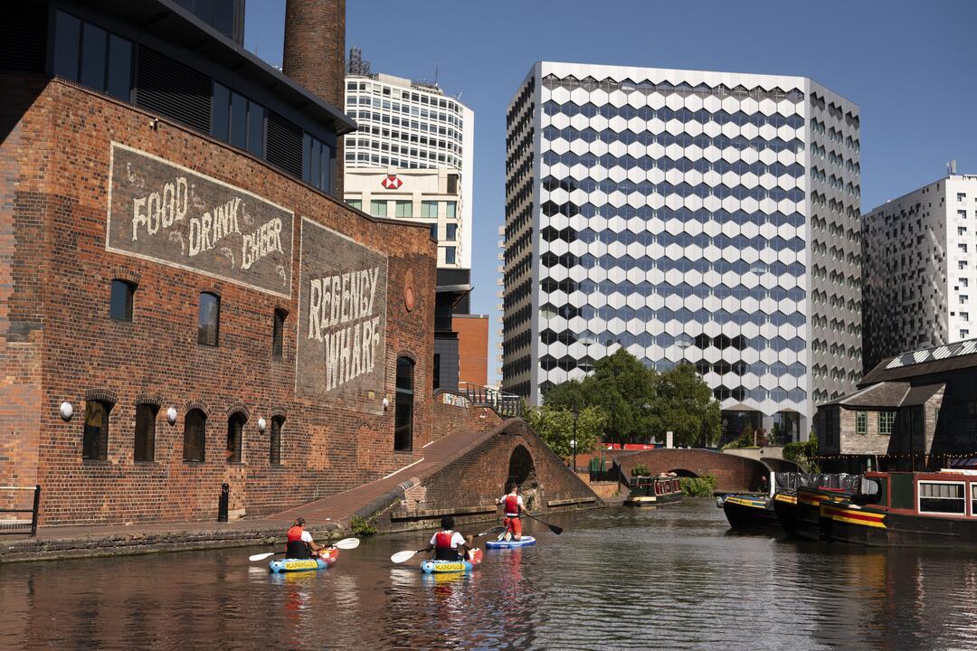 Group of people paddleboarding past industrial buildings on a canal