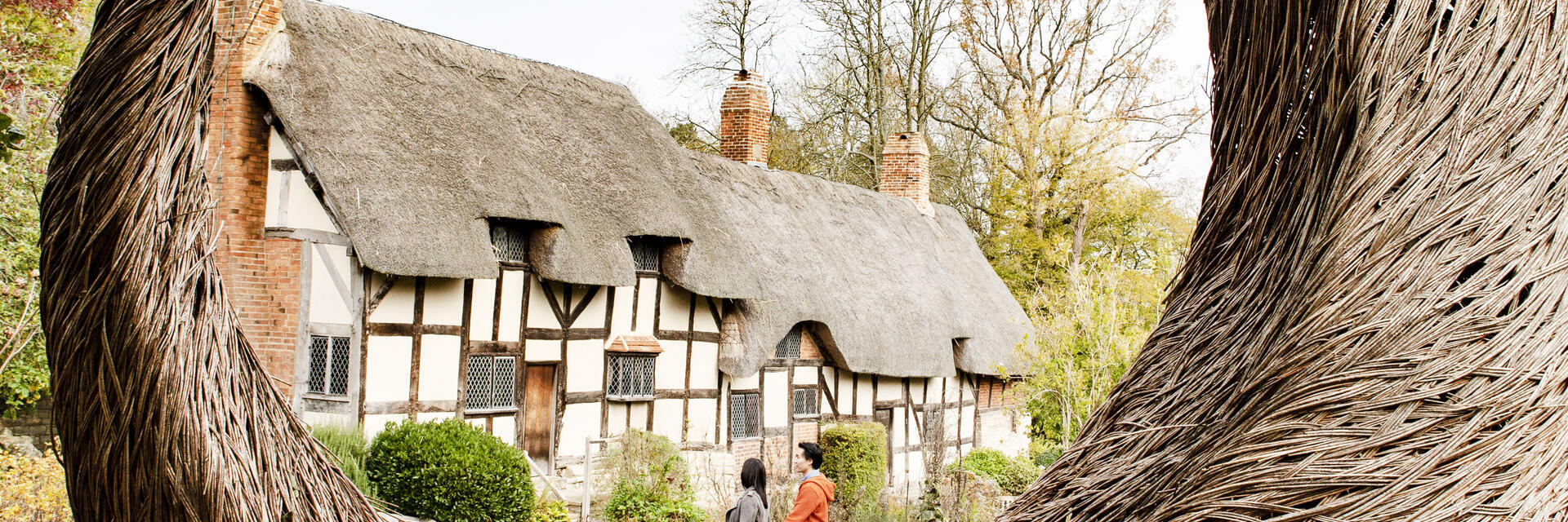 زوجان يمشيان بالقرب من كوخ يظهر من خلال منحوتة كبيرة على شكل هلال من خشب الصفصاف في حديقة