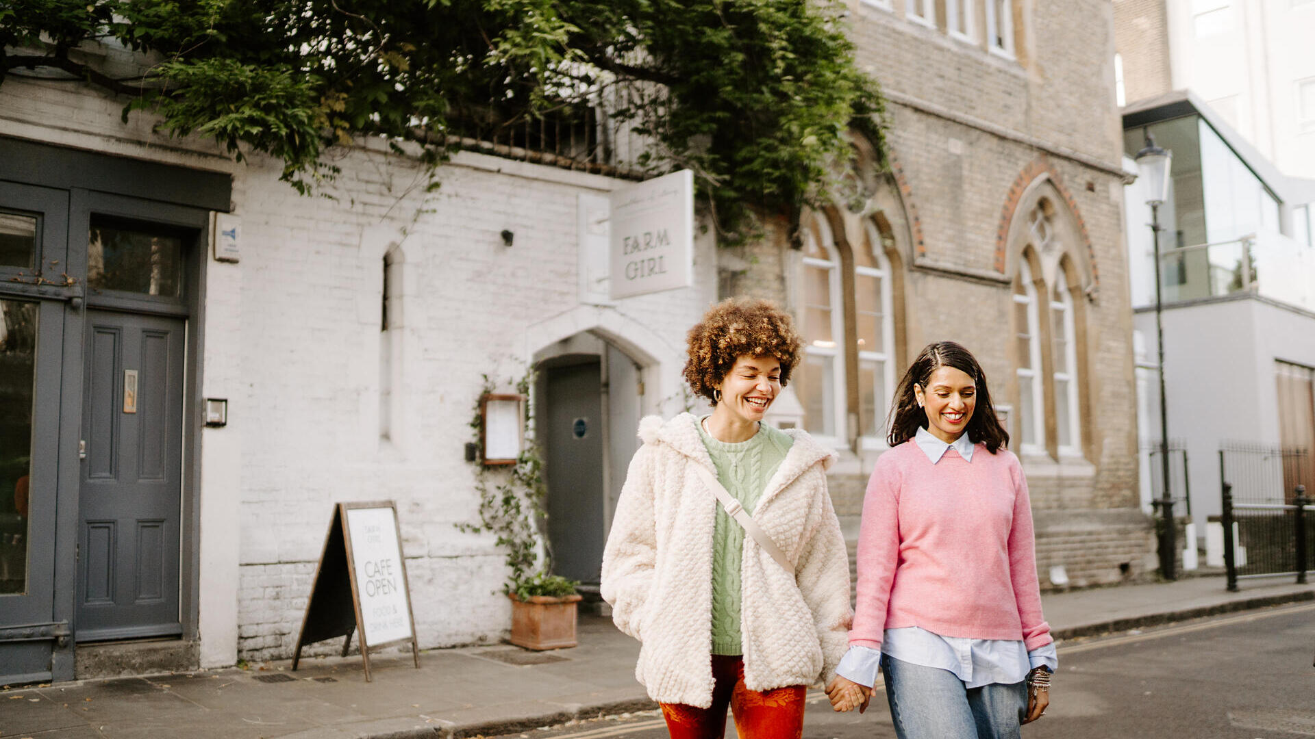 Zwei Frauen gehen auf der Straße vor einem Café neben einem Backsteingebäude.