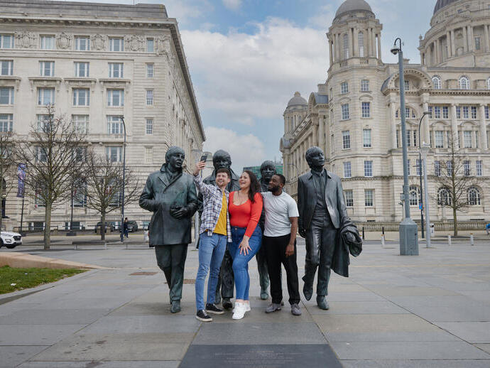 Eine Gruppe von Freunden, zwei Männer und eine Frau, machen ein Selfie vor einer Statue im Stadtzentrum.