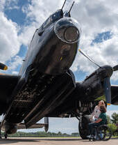 A man in a wheelchair and a woman look up to an old propeller aeroplane
