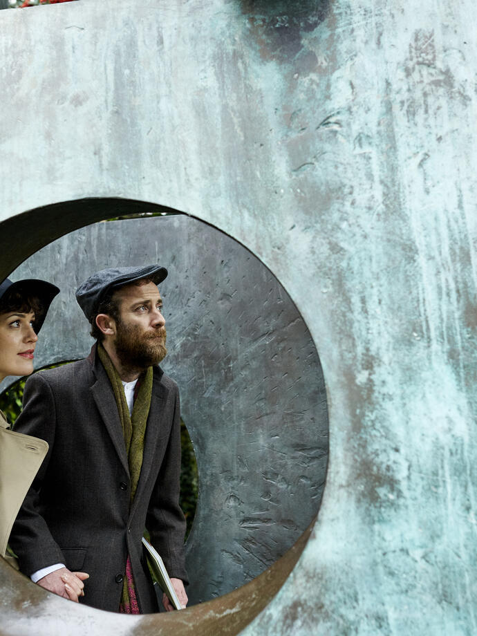 Pareja vista a través de un hueco en una gran escultura de bronce en un jardín