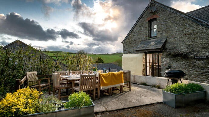 Mobiliario de comedor de madera al aire libre para diez personas, con barbacoa, vajilla y una alfombra.