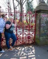 Two women pose in front of the red gates at the Strawberry Field garden.