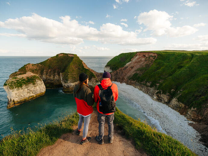 A man and woman stand on a cliff edge in front of a sea view