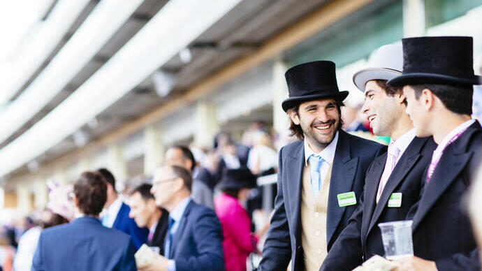Two men smiling wearing formal dress in a busy grandstand at a horse racecourse