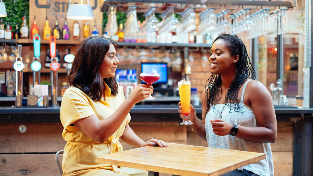 Two women sat at a table beside the bar, raising glasses