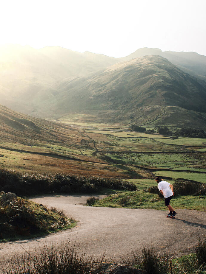 Man skateboarding down a road through a deep valley in the sunshine